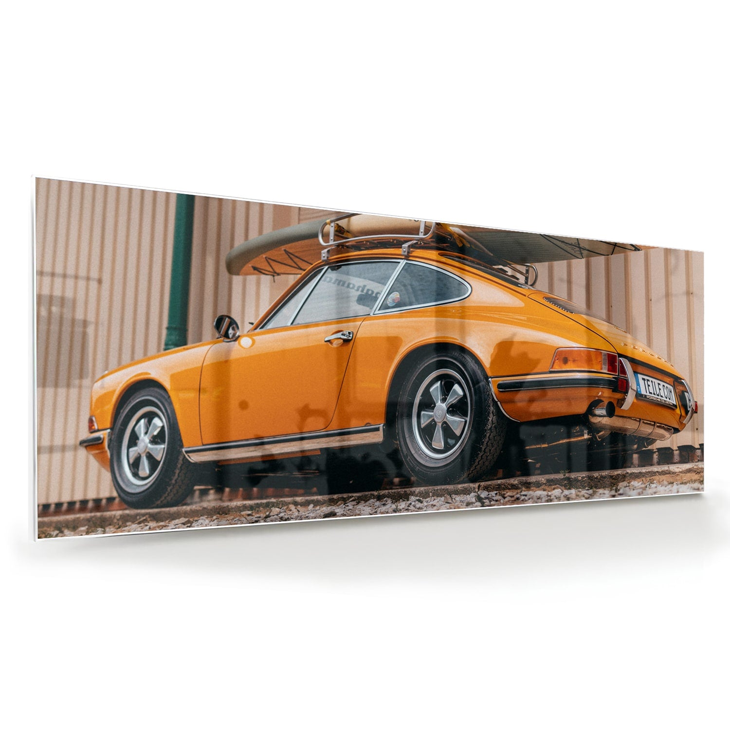 Een glazen schilderij van een oranje auto met een surfbord op het dak, gepresenteerd in een moderne woonkamer.