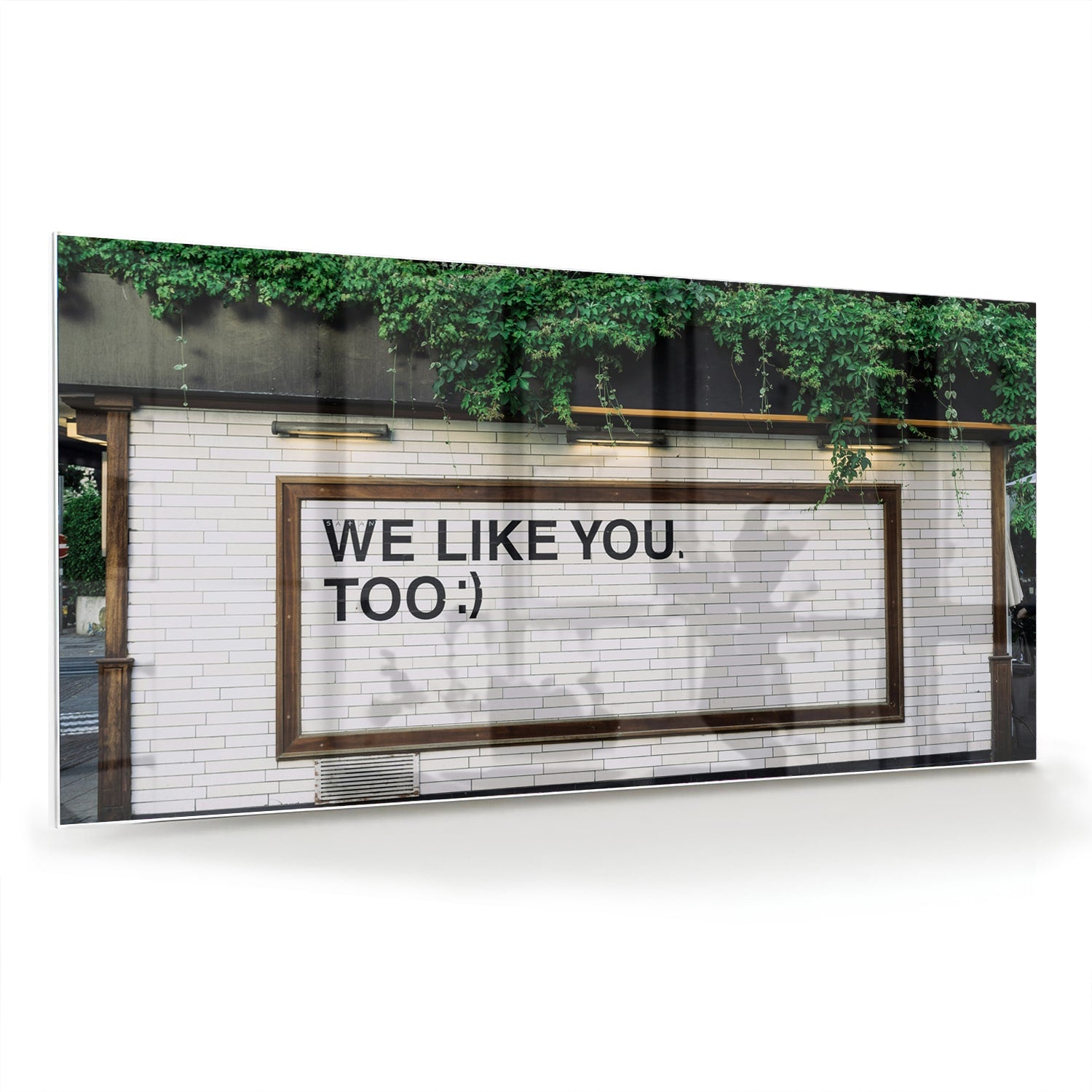 Glas schilderij met de tekst 'We Like You Too' en groene planten achtergronden.