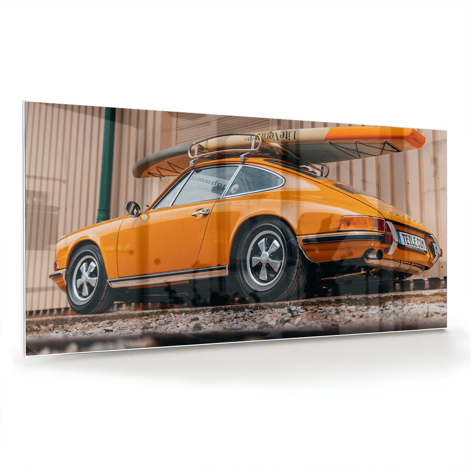 Een glazen schilderij van een oranje auto met een surfbord op het dak, gepresenteerd in een moderne woonkamer.