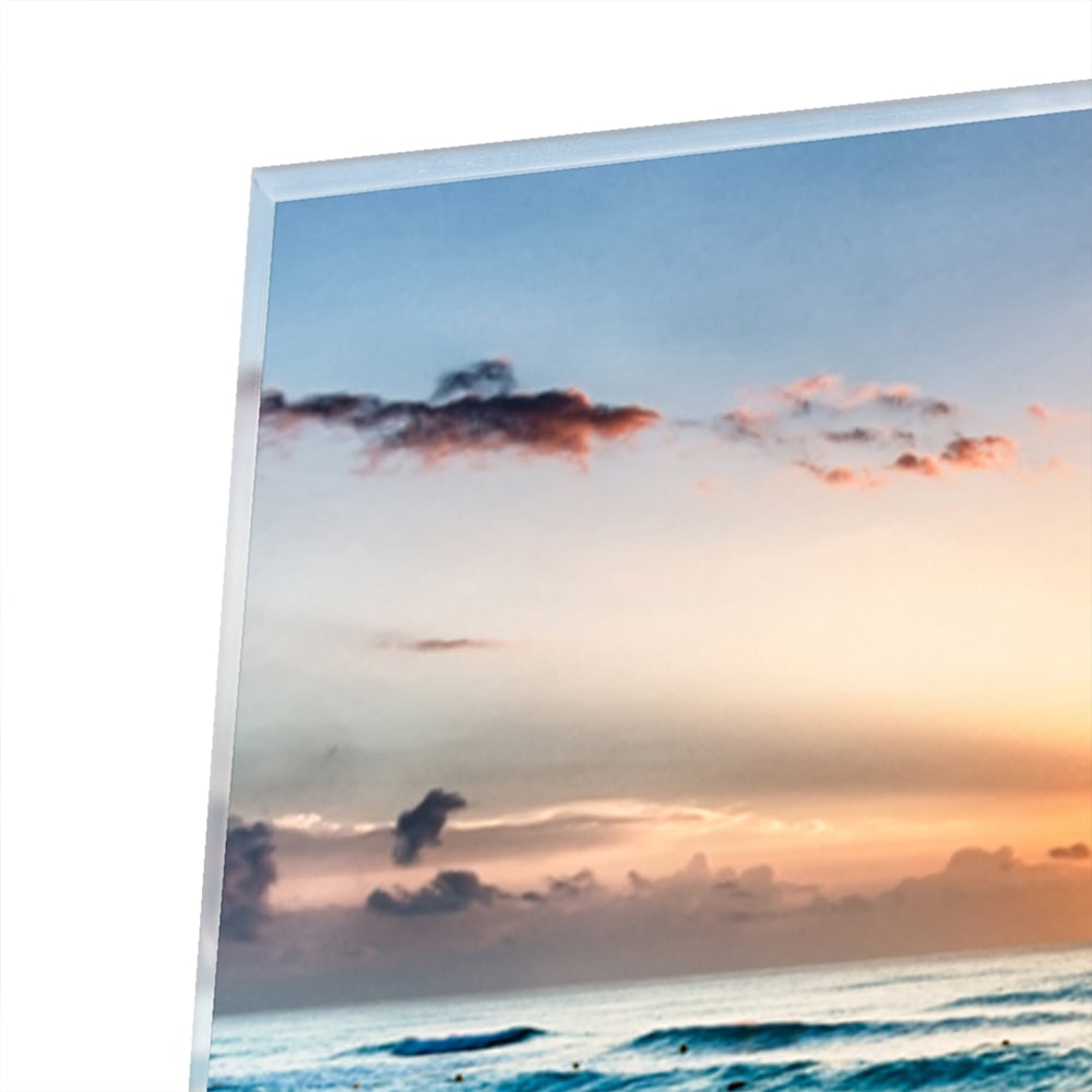 Glazen schilderij van een zonsondergang boven de zee, met kalme golven en zand.