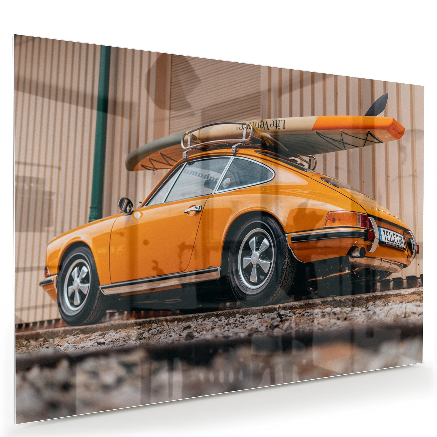 Een glazen schilderij van een oranje auto met een surfbord op het dak, gepresenteerd in een moderne woonkamer.