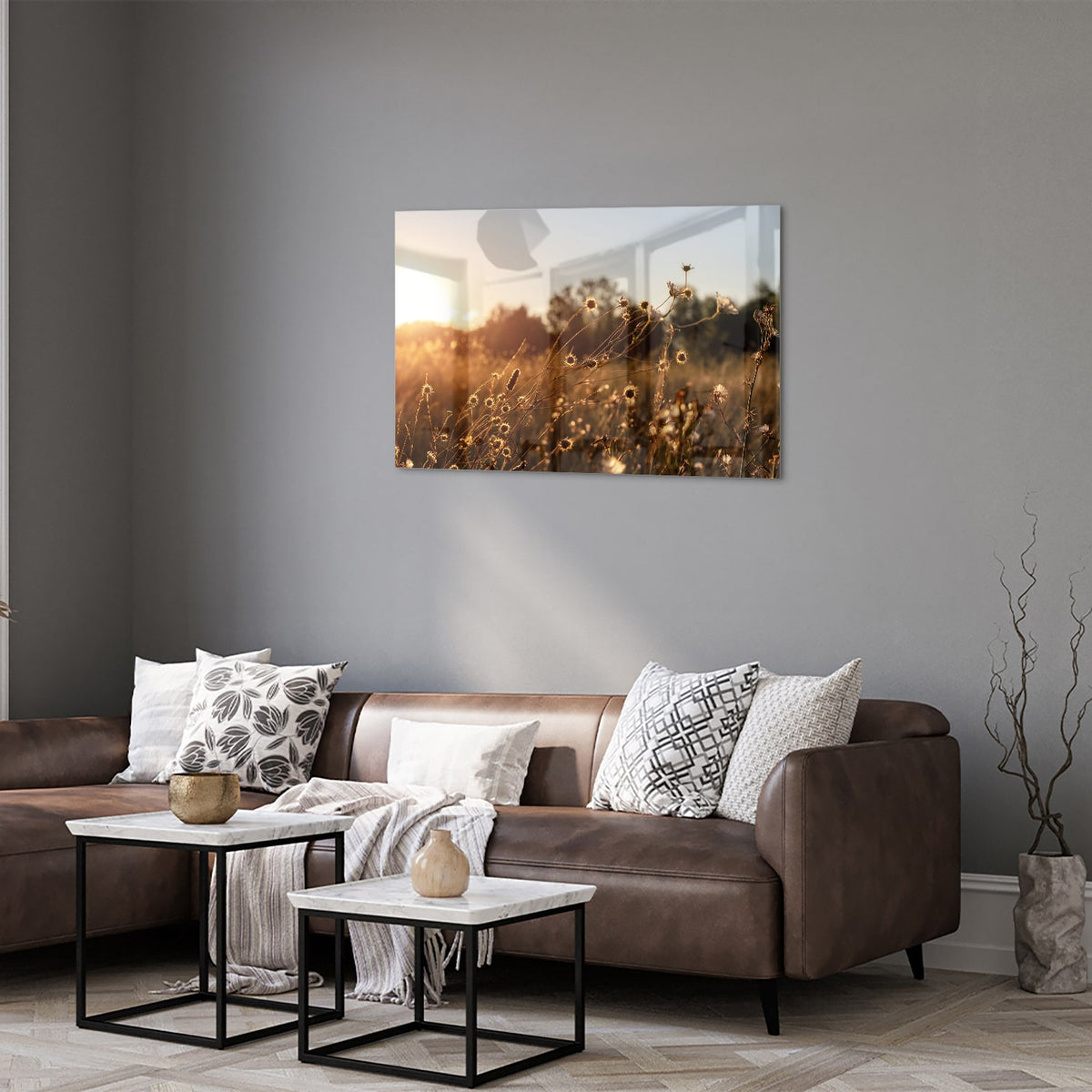 Glazen schilderij van een zonsondergang met bloeiende bloemen, hangend aan een witte muur.