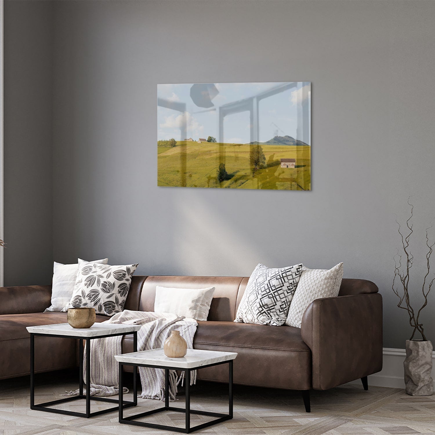 Glazen schilderij met groene heuvels en boerderijen op een witte muur.