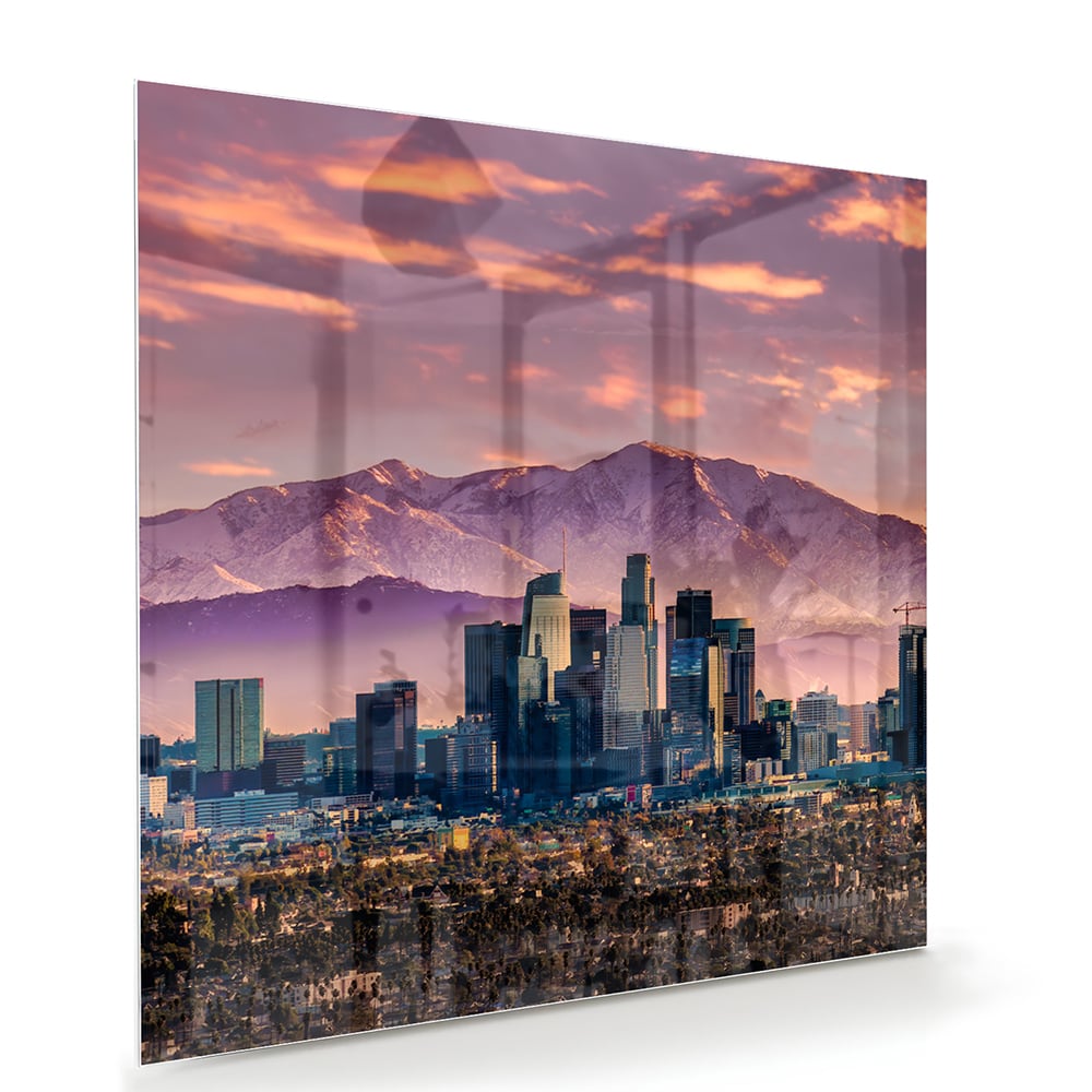 Glazen schilderij van een stadspanorama bij zonsondergang met bergen op de achtergrond.