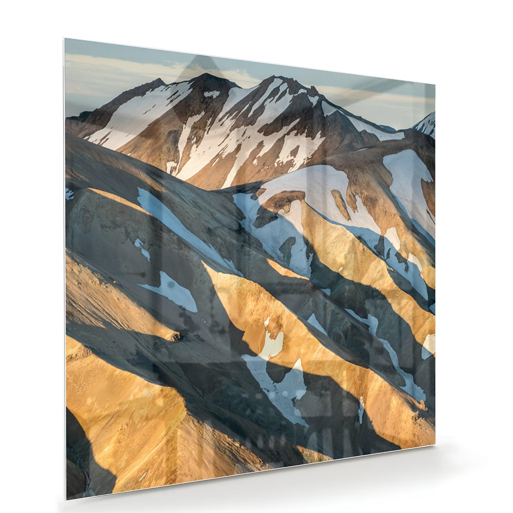 Glazen schilderij van bergen in blauw en goud, hanging in een stijlvolle kamer.