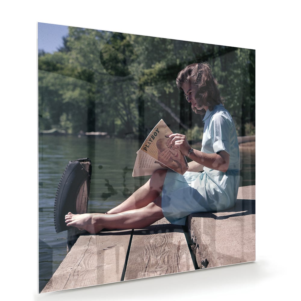 Glazen schilderij van een vrouw die aan het water leest in een serene omgeving.