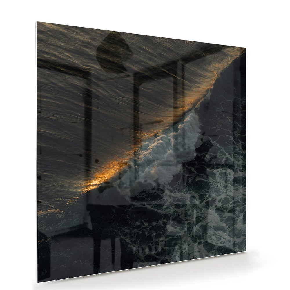 Zwart glazen schilderij van een zeegezicht met gouden accenten, hangt aan een lichtgekleurde muur.