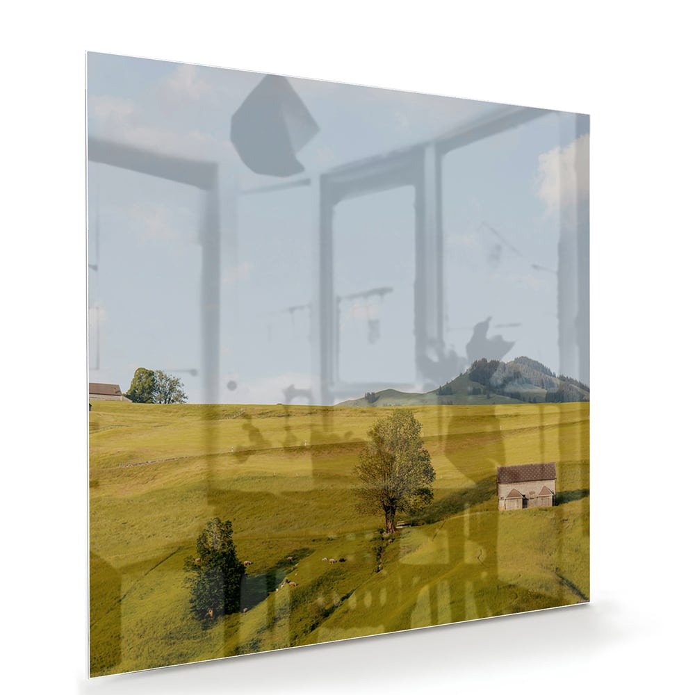 Glazen schilderij met groene heuvels en boerderijen op een witte muur.