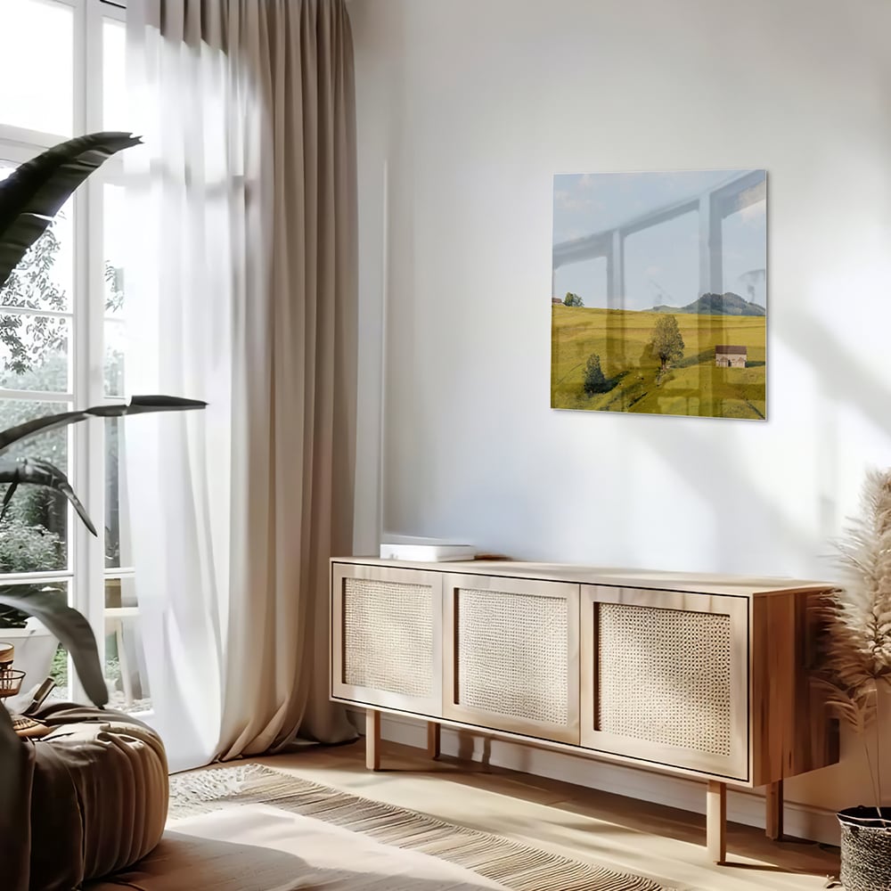 Glazen schilderij met groene heuvels en boerderijen op een witte muur.