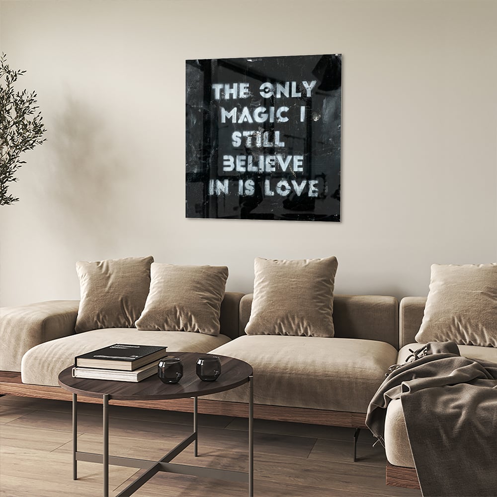 Glazen schilderij met de tekst 'The only magic I still believe in is love', hangt aan de muur in een lichte woonkamer.