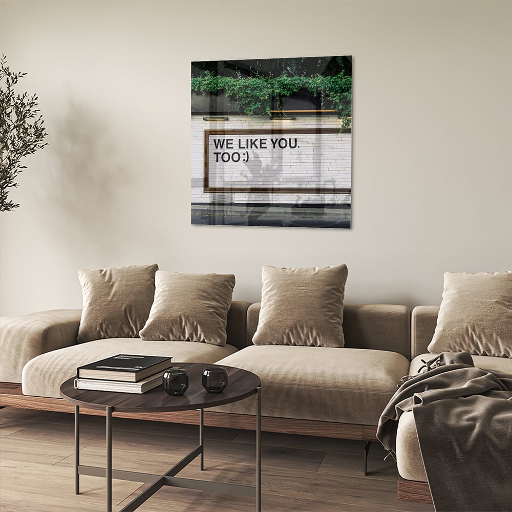 Glas schilderij met de tekst 'We Like You Too' en groene planten achtergronden.