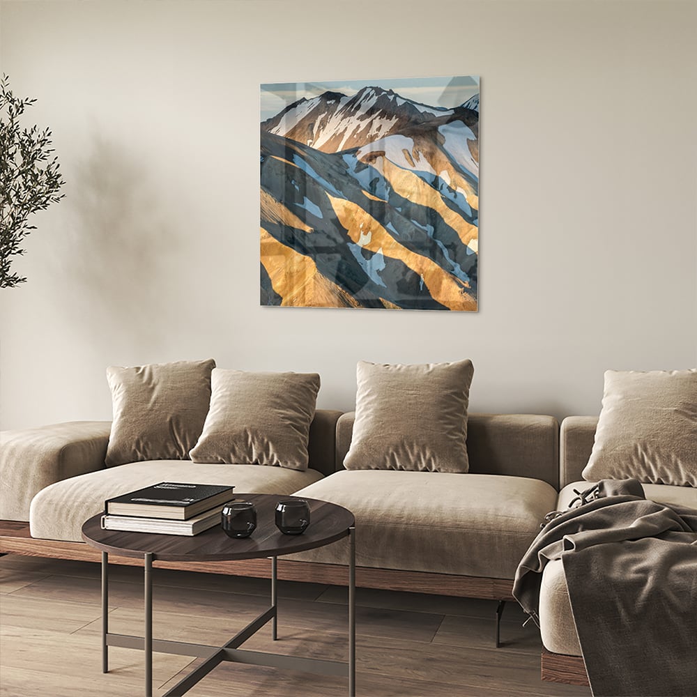 Glazen schilderij van bergen in blauw en goud, hanging in een stijlvolle kamer.