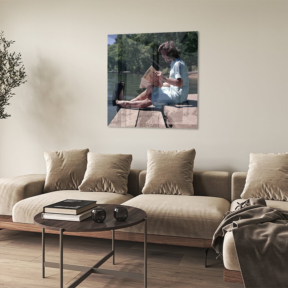 Glazen schilderij van een vrouw die aan het water leest in een serene omgeving.