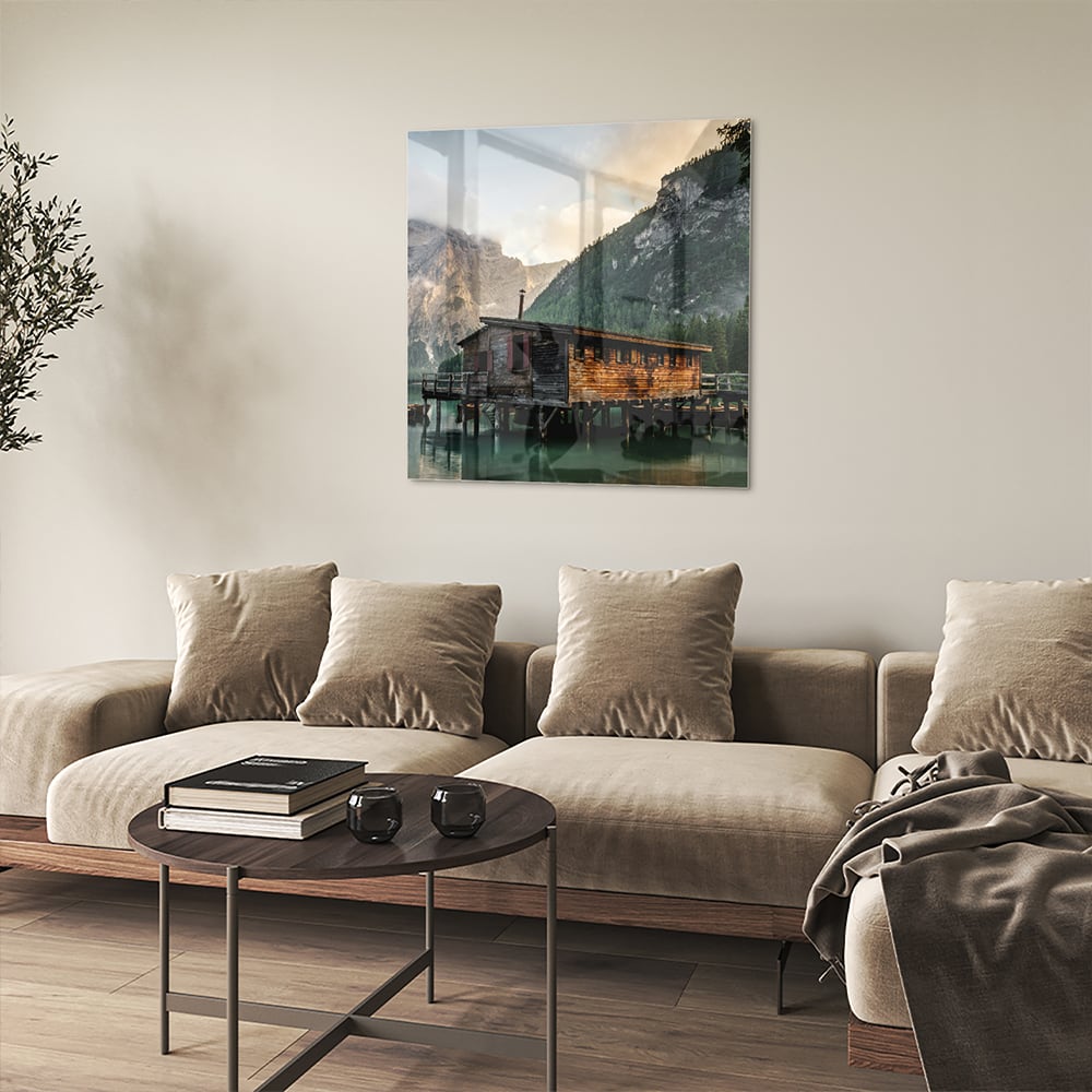 Glazen schilderij van een berghut aan een kalm meer met bergen op de achtergrond.