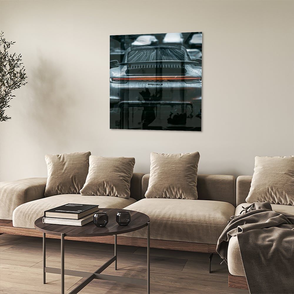 Glazen schilderij van een sportwagen aan de muur in een lichte woonkamer.