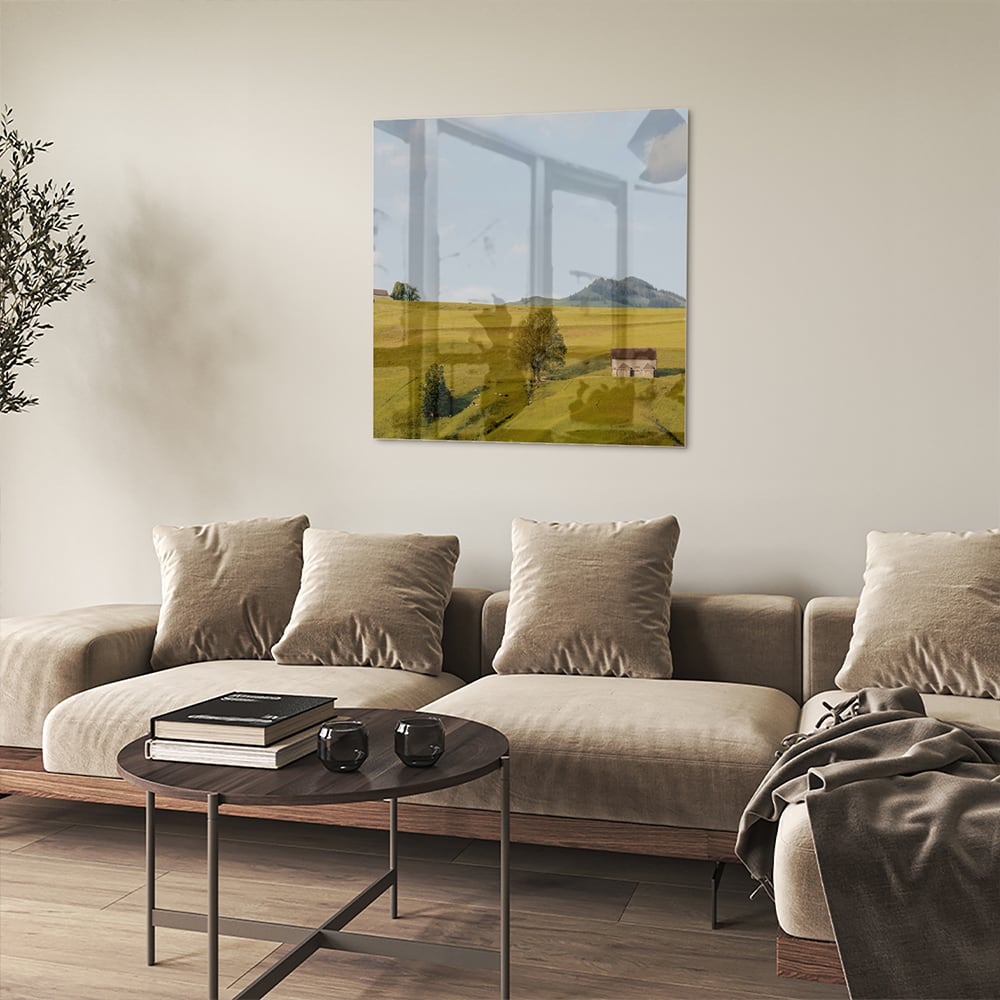 Glazen schilderij met groene heuvels en boerderijen op een witte muur.