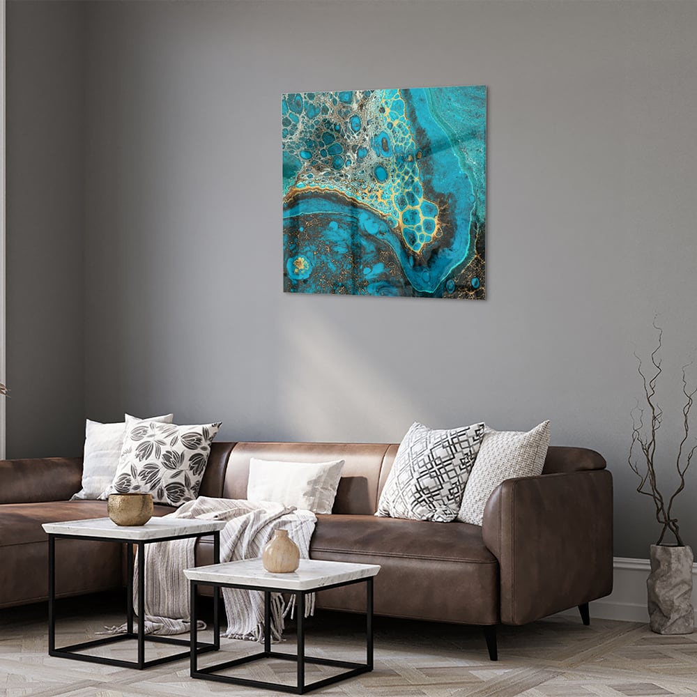 Glazen schilderij in turkoois met gouden accenten aan de muur boven een houten meubel.