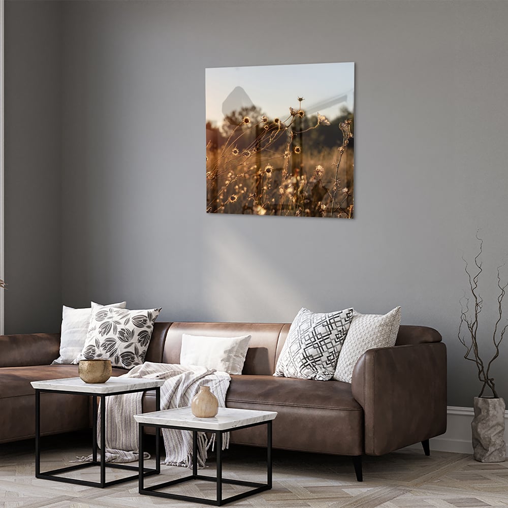 Glazen schilderij van een zonsondergang met bloeiende bloemen, hangend aan een witte muur.