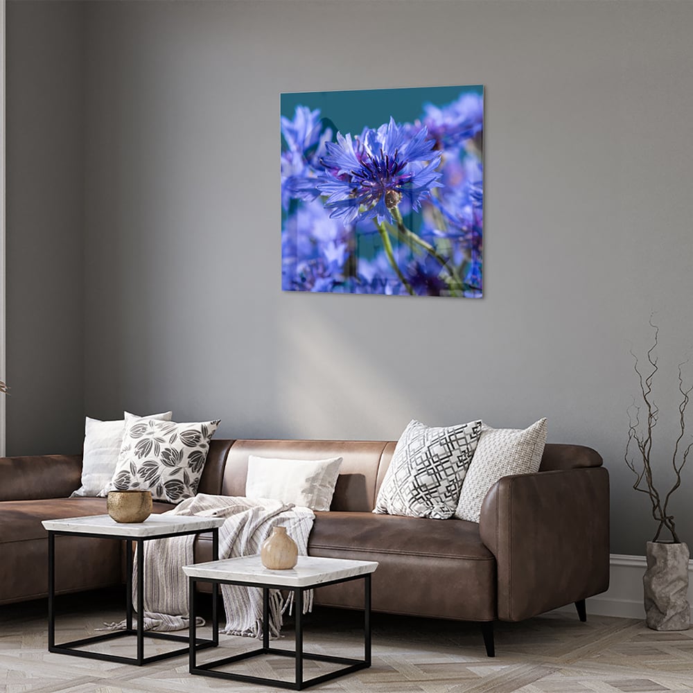 Een glazen schilderij met paarse bloemen op een witte muur, in een sfeervolle woonkamer.