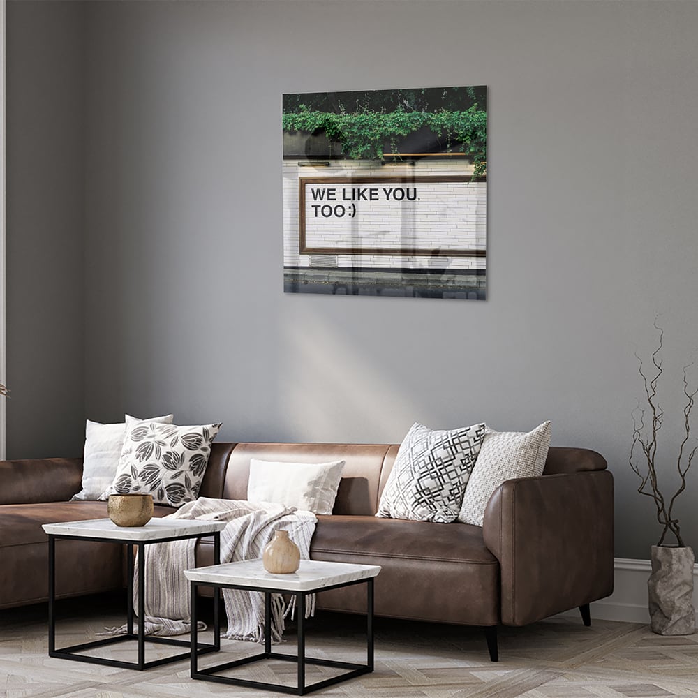 Glas schilderij met de tekst 'We Like You Too' en groene planten achtergronden.