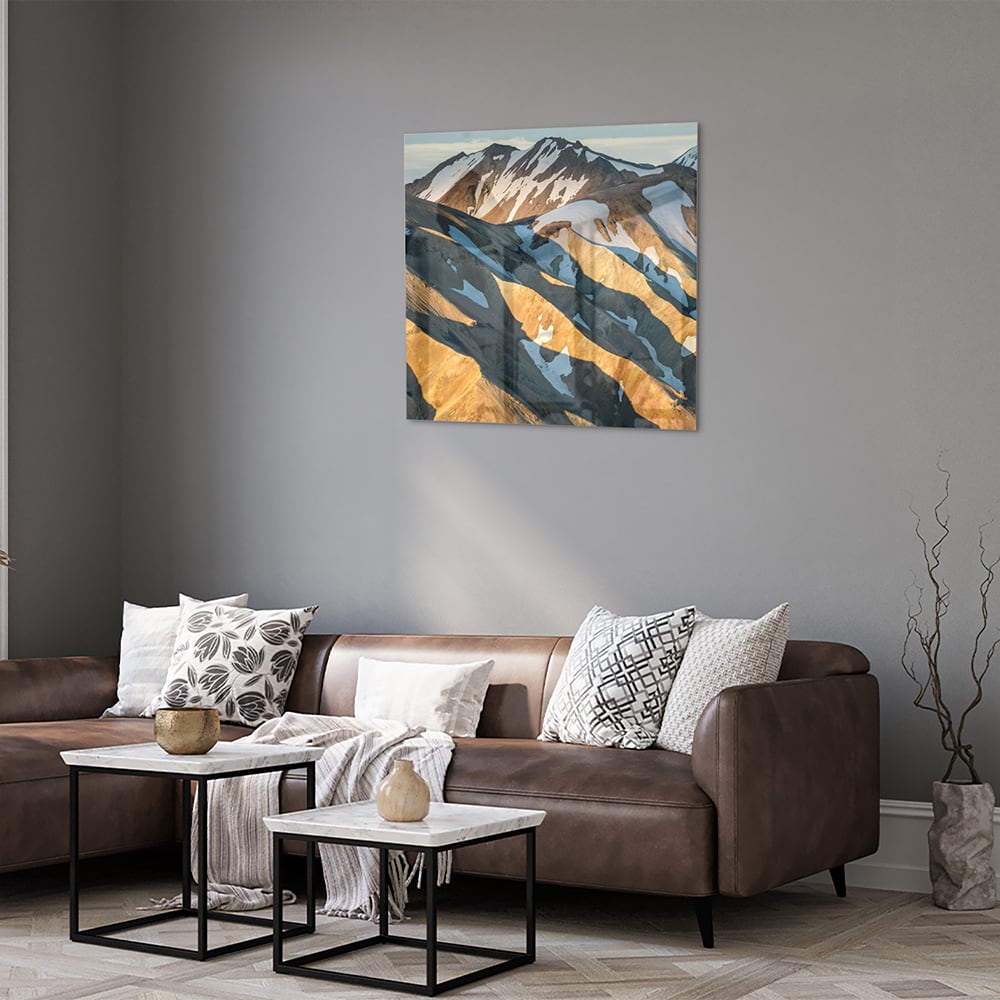 Glazen schilderij van bergen in blauw en goud, hanging in een stijlvolle kamer.