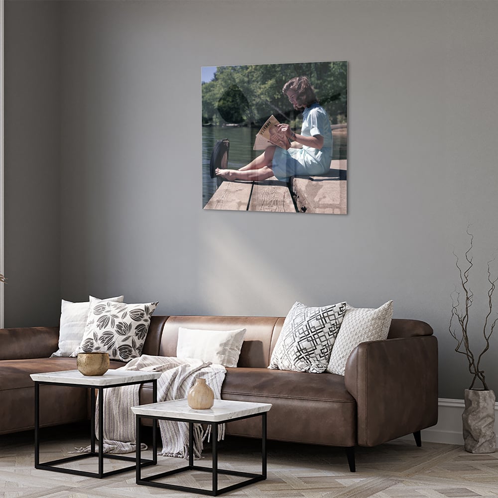 Glazen schilderij van een vrouw die aan het water leest in een serene omgeving.