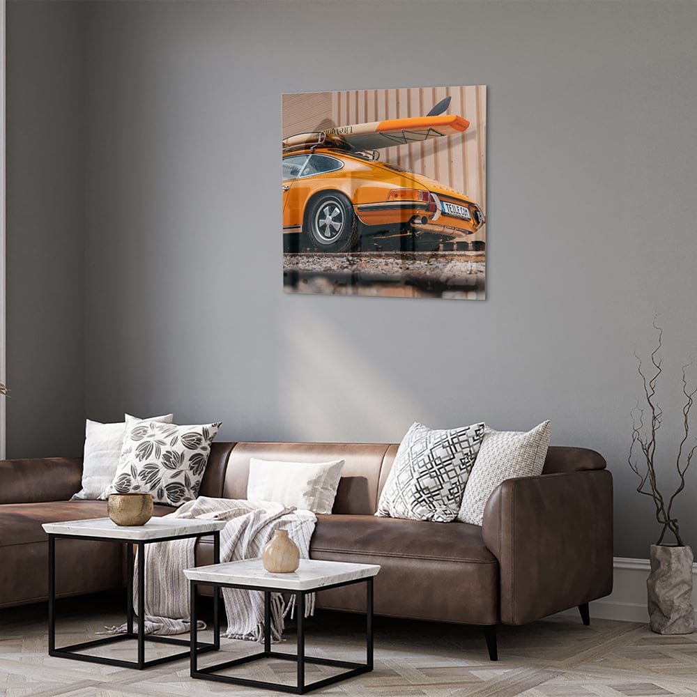 Een glazen schilderij van een oranje auto met een surfbord op het dak, gepresenteerd in een moderne woonkamer.