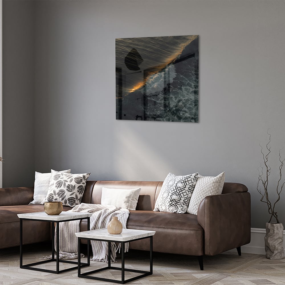 Zwart glazen schilderij van een zeegezicht met gouden accenten, hangt aan een lichtgekleurde muur.