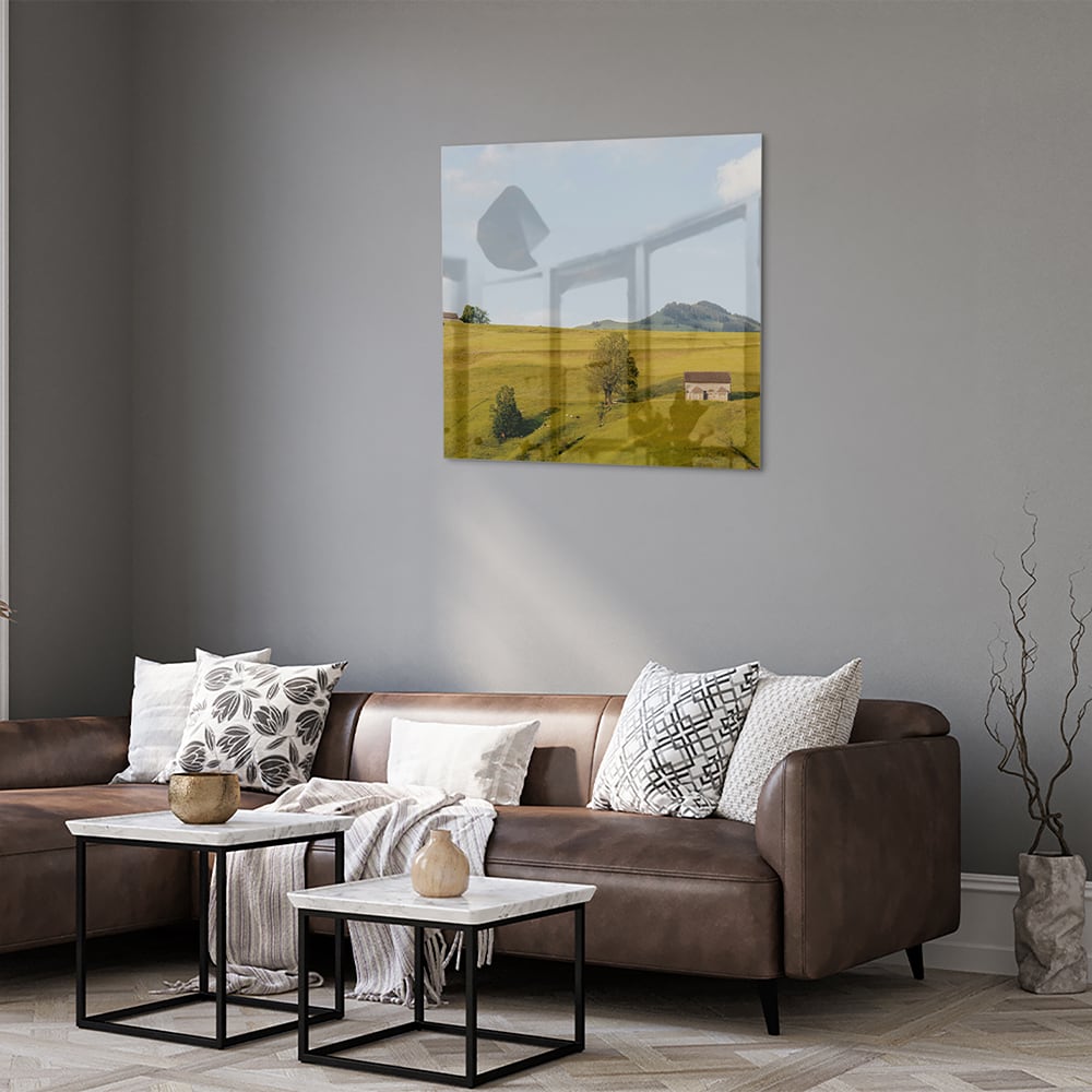 Glazen schilderij met groene heuvels en boerderijen op een witte muur.