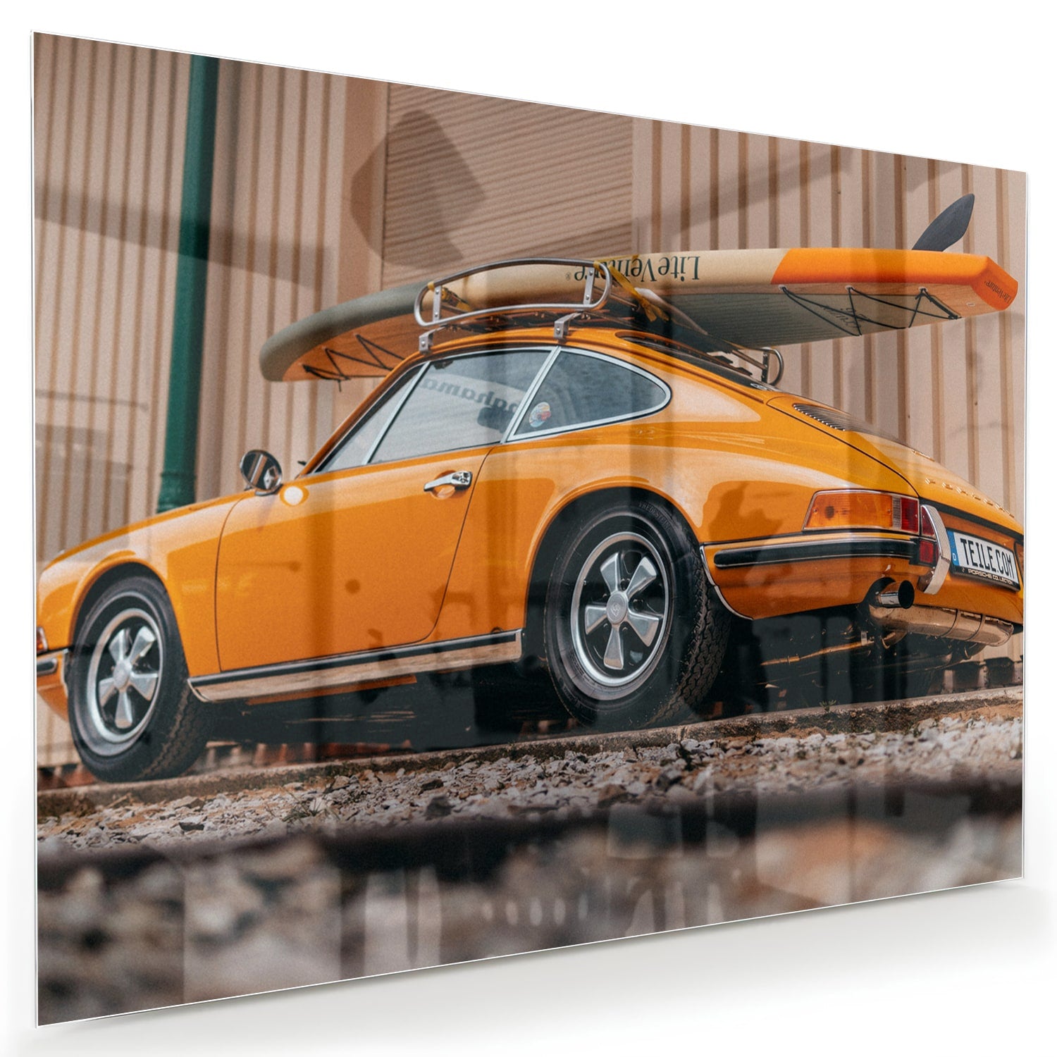 Een glazen schilderij van een oranje auto met een surfbord op het dak, gepresenteerd in een moderne woonkamer.