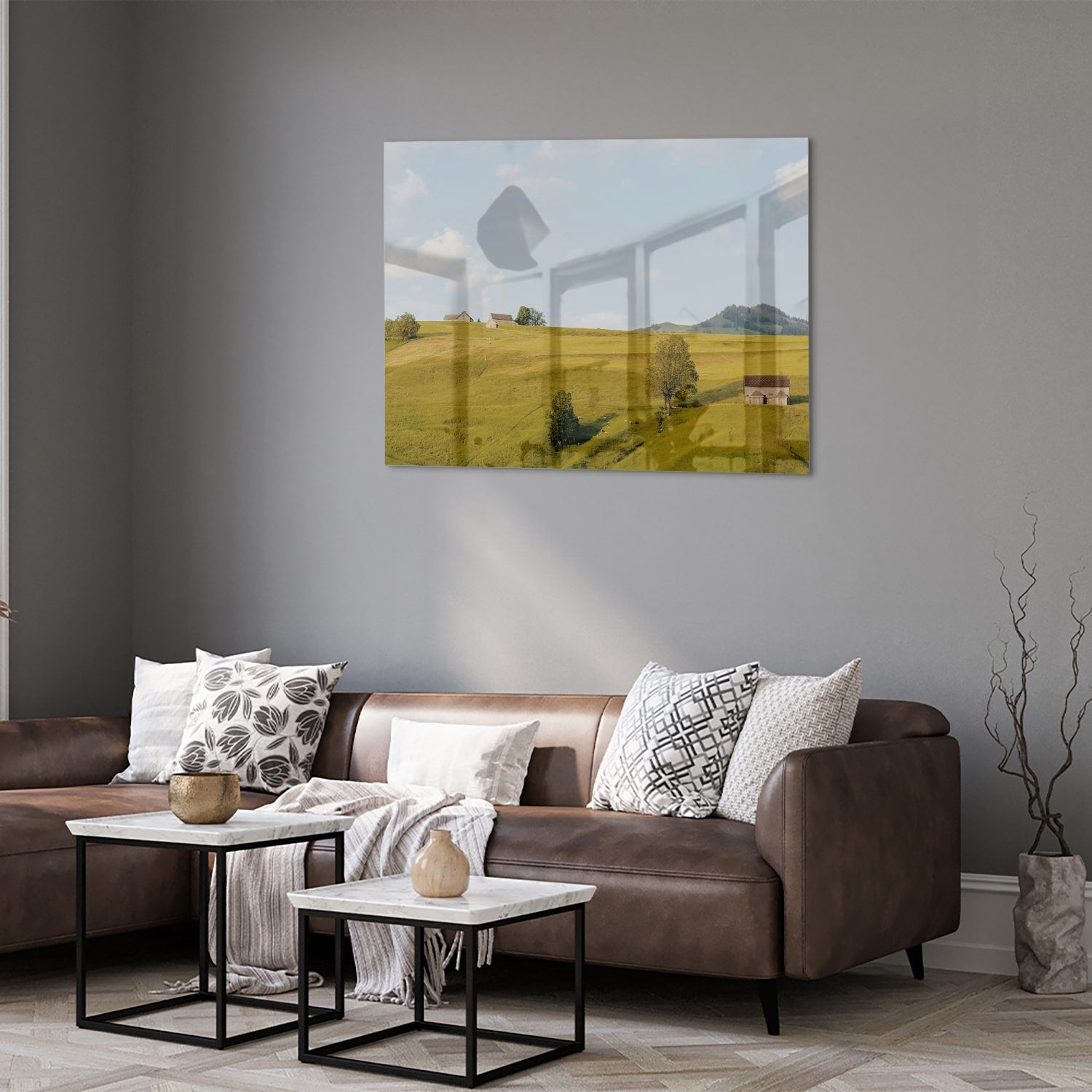 Glazen schilderij met groene heuvels en boerderijen op een witte muur.