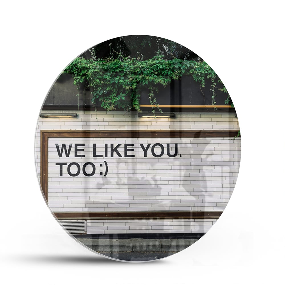 Glas schilderij met de tekst 'We Like You Too' en groene planten achtergronden.