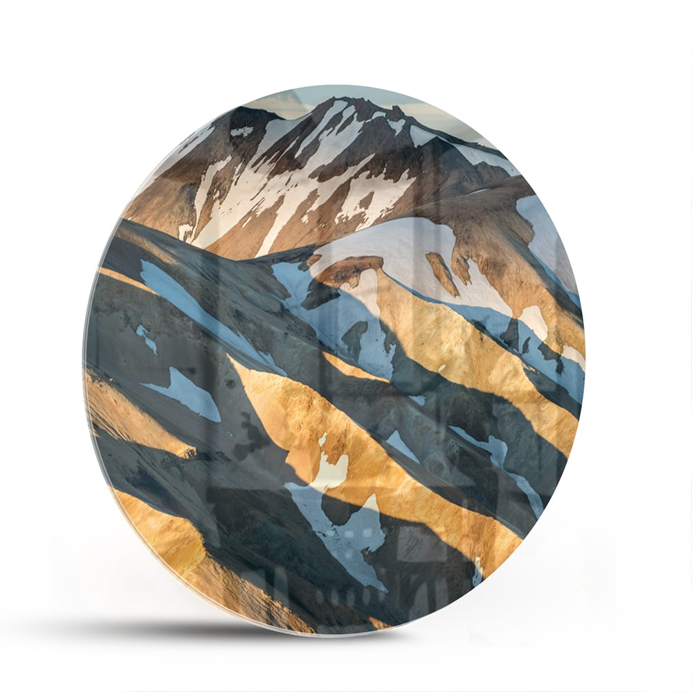 Glazen schilderij van bergen in blauw en goud, hanging in een stijlvolle kamer.