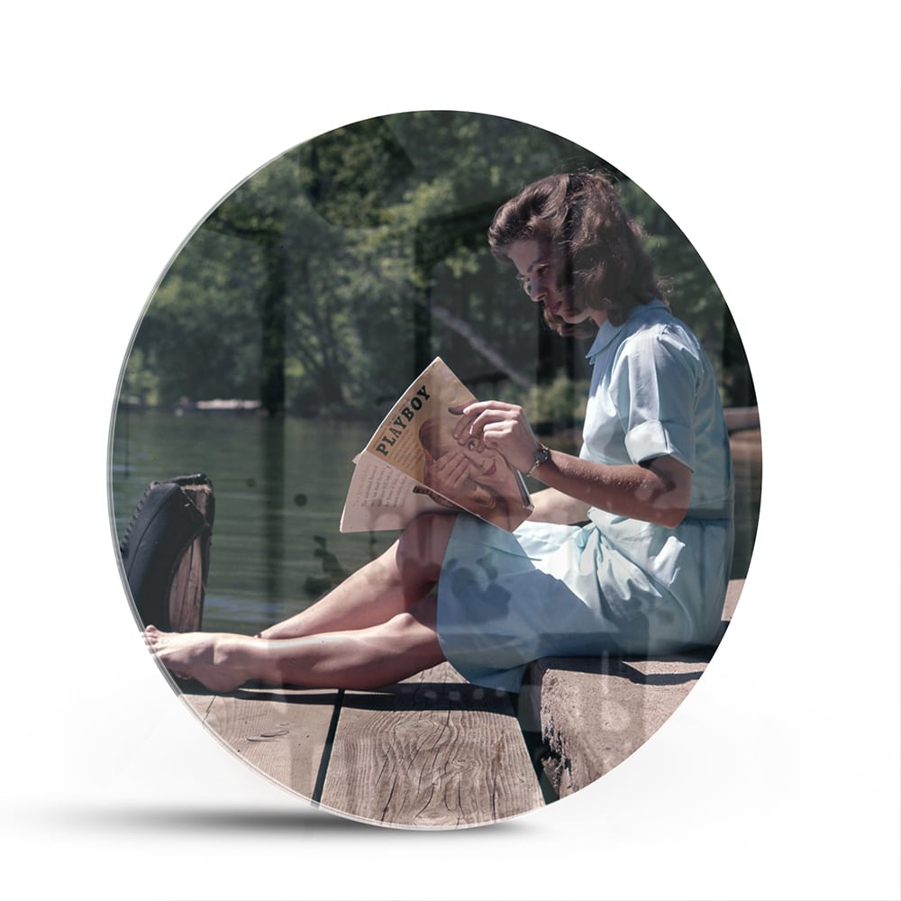 Glazen schilderij van een vrouw die aan het water leest in een serene omgeving.
