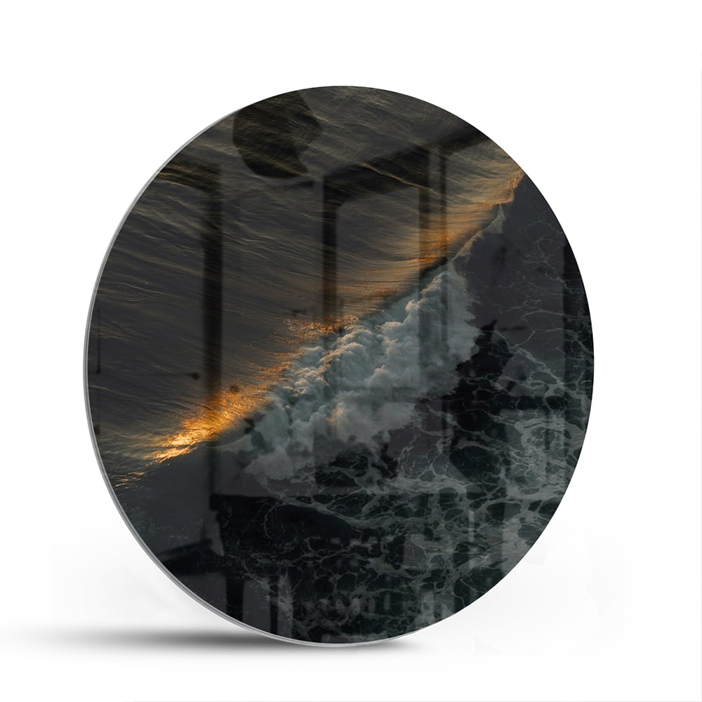 Zwart glazen schilderij van een zeegezicht met gouden accenten, hangt aan een lichtgekleurde muur.