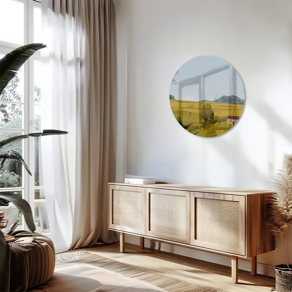 Glazen schilderij met groene heuvels en boerderijen op een witte muur.