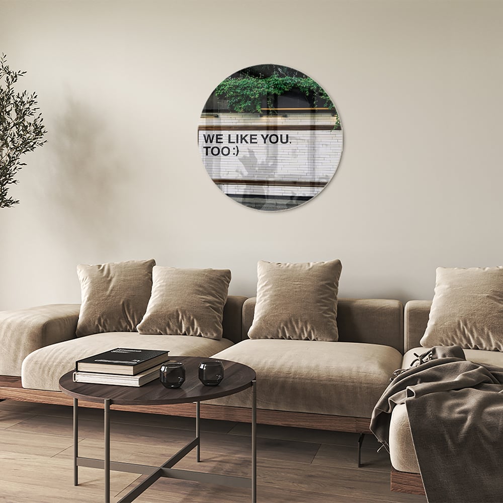 Glas schilderij met de tekst 'We Like You Too' en groene planten achtergronden.