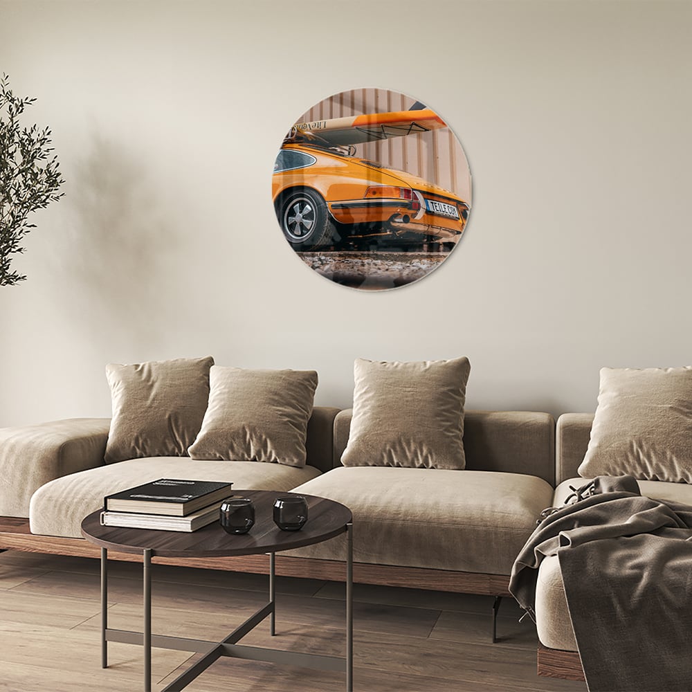 Een glazen schilderij van een oranje auto met een surfbord op het dak, gepresenteerd in een moderne woonkamer.