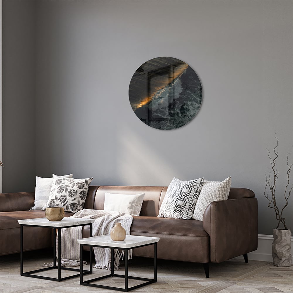 Zwart glazen schilderij van een zeegezicht met gouden accenten, hangt aan een lichtgekleurde muur.